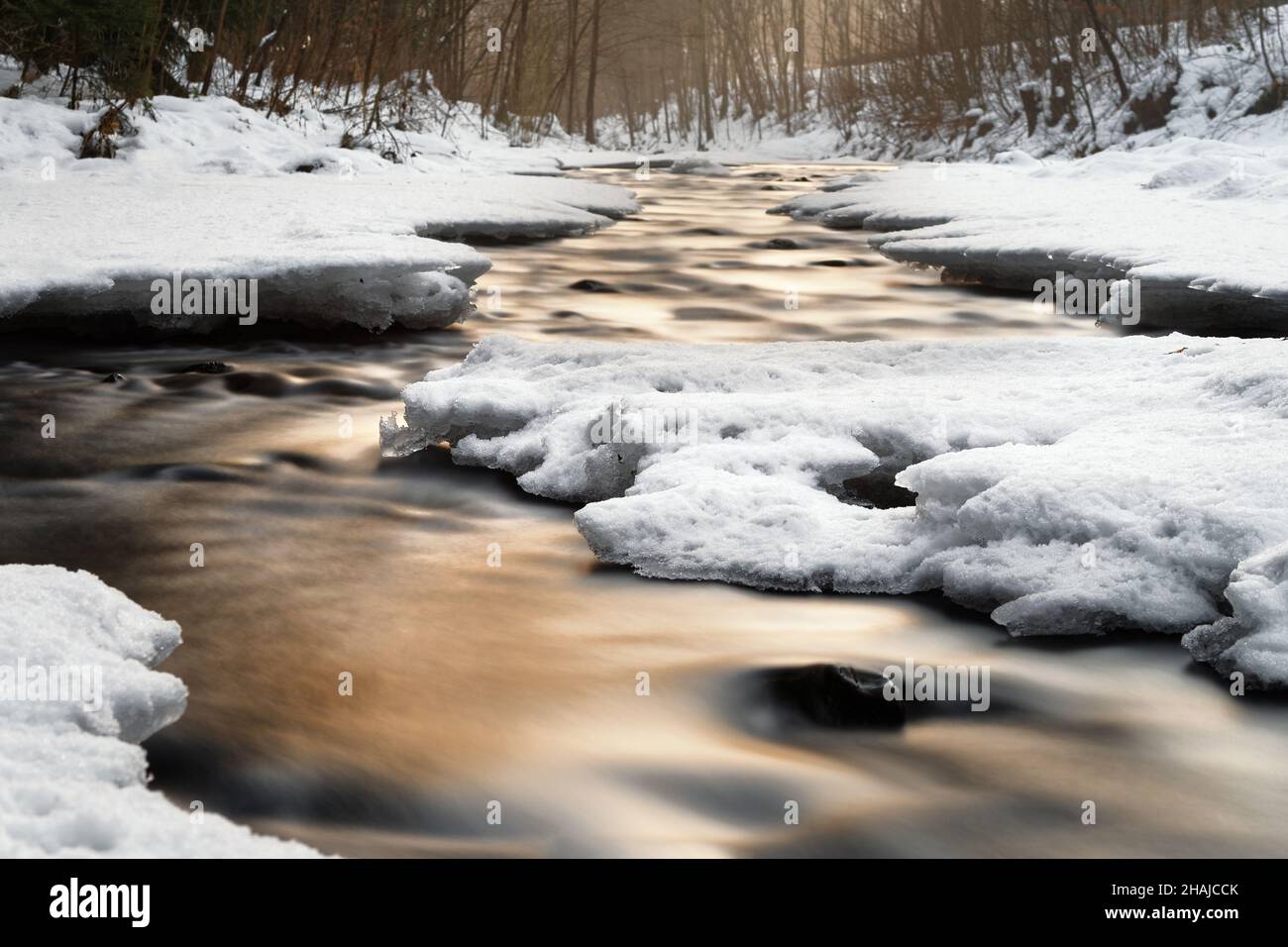 Wintery river view with reflection of colored atmospheric evening light, snow and ice on the shore, water movement in long exposure - Location: German Stock Photo