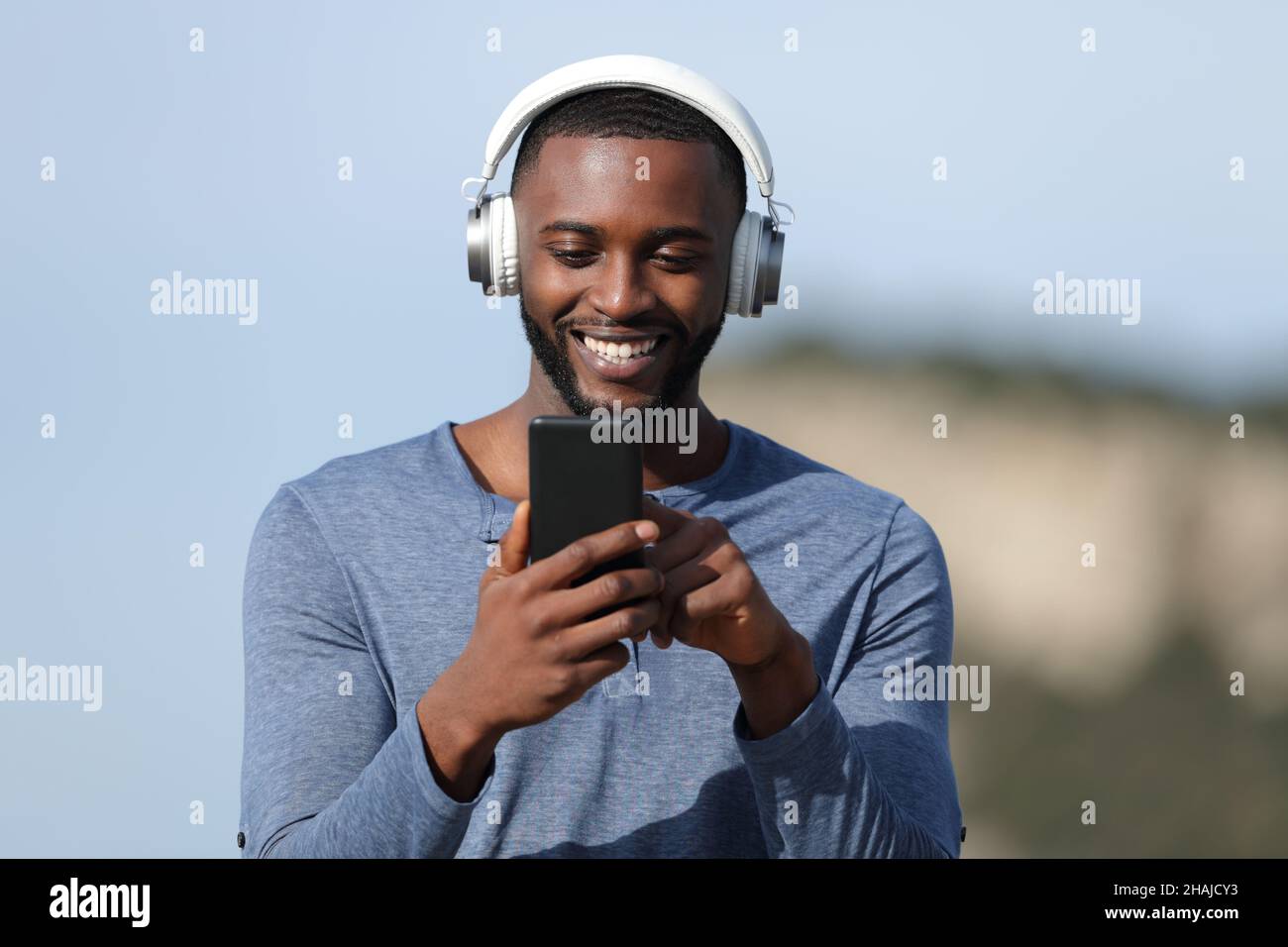 Front view portrait of a happy man with black skin listening to music in the mountain Stock Photo