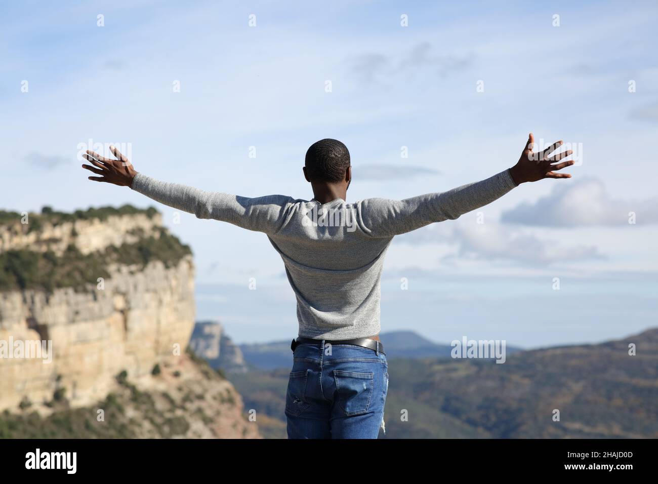 Back view portrait of a happy man with black skin celebrating outstretching arms in the mountain Stock Photo