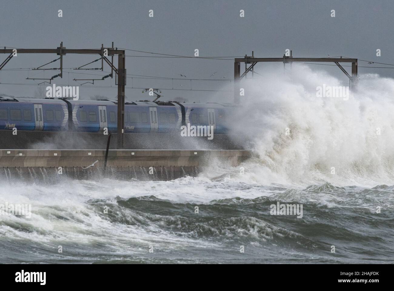 Wave crashes over road and railway line as ScotRail train at Saltcoats as a ScotRail train passes by during bad weather, Saltcoats, Scotland, UK Stock Photo