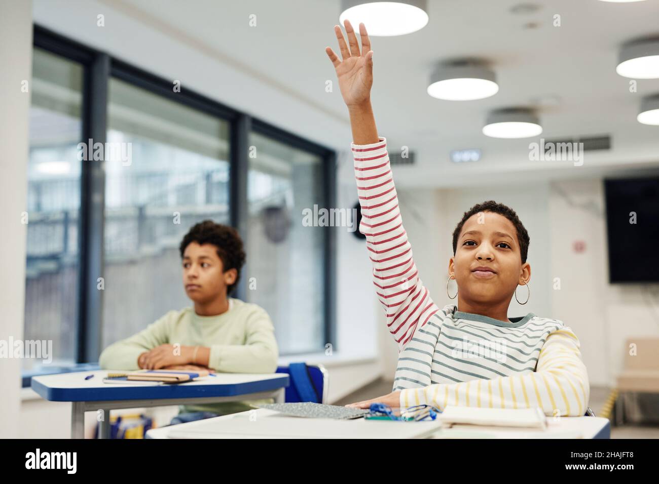 Portrait of African-American girl with short hair raising hand in modern classroom, copy space Stock Photo