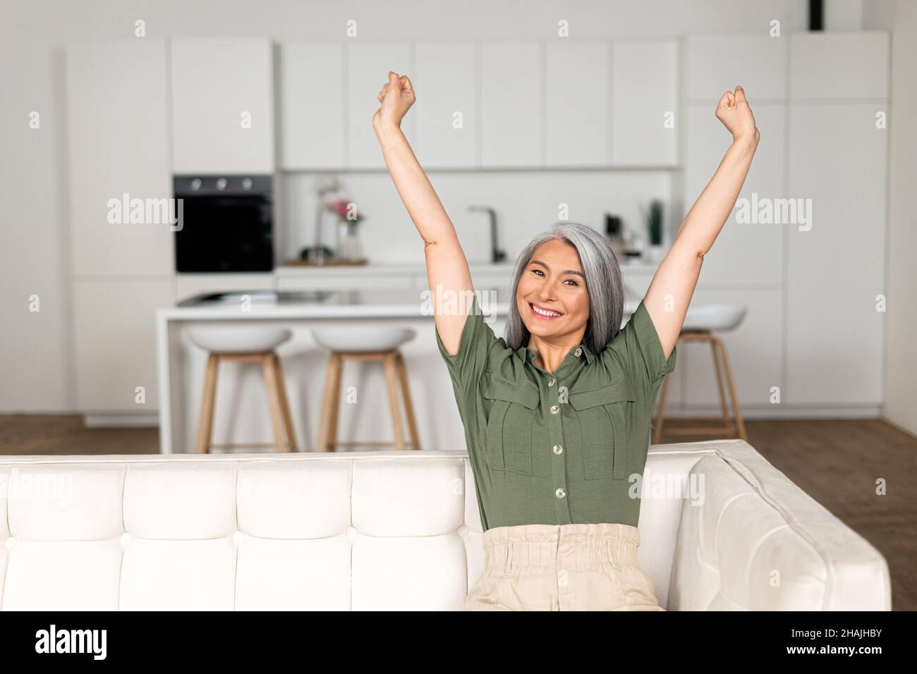 Gray-haired woman stretching arms sitting on the sofa at home, cheerful ...