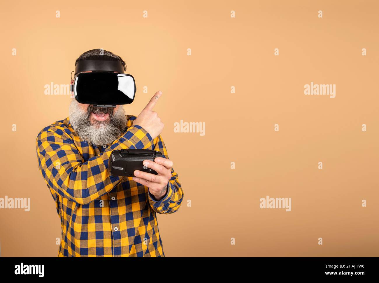gamer in VR glasses on a yellow background holds a device and points his fingers to a place for text, a man with wireless gadgets for virtual reality Stock Photo