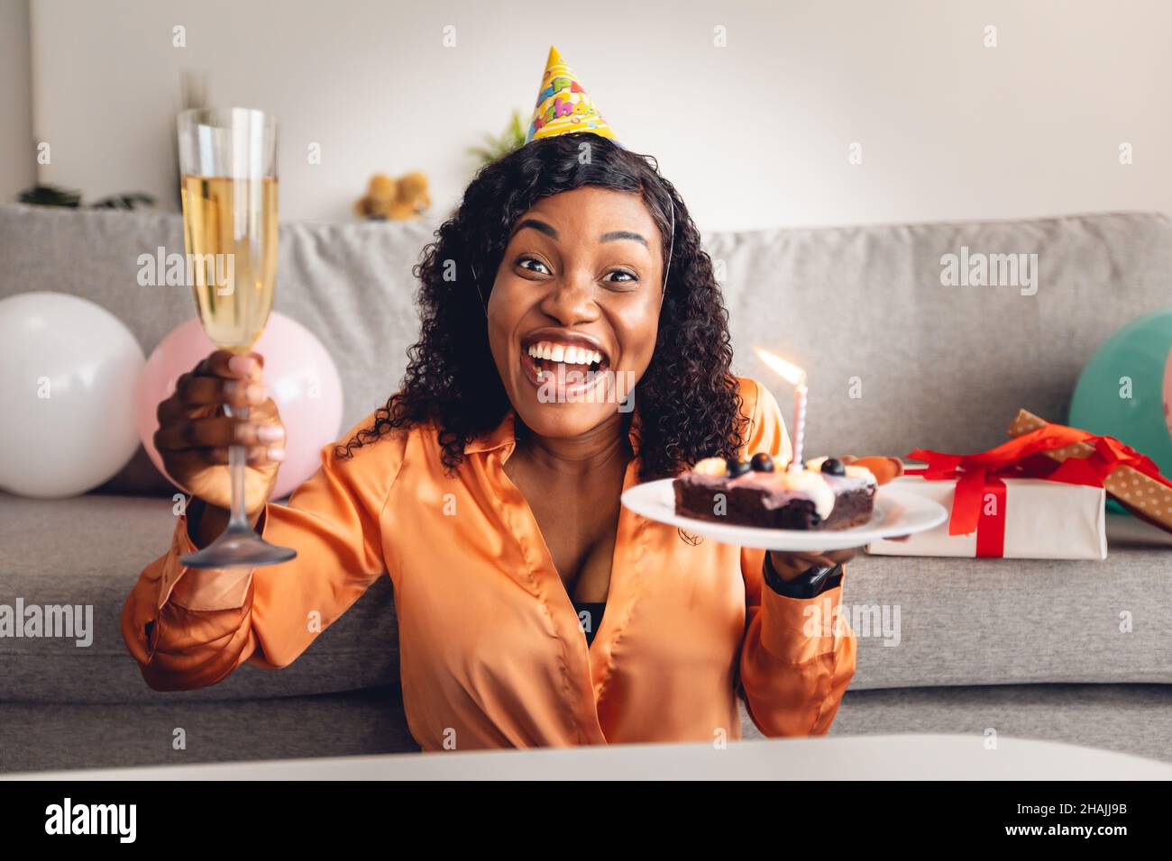 Joyful Black Lady Holding Birthday Cake And Glass At Home Stock Photo