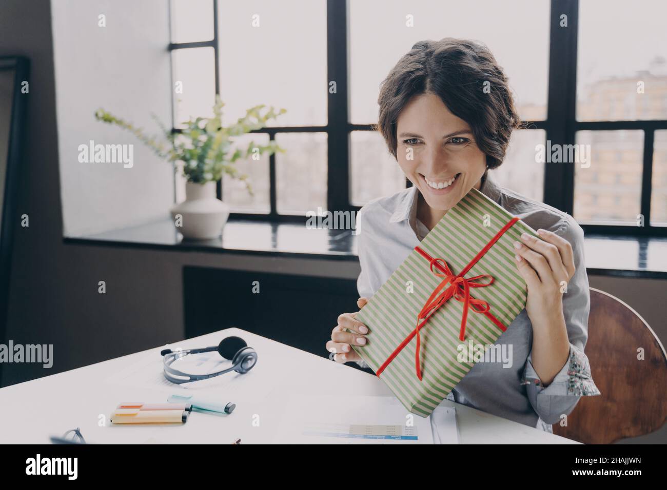 Cheerful lady office employee looking at screen broadly smiling showing to computer camera Xmas gift Stock Photo
