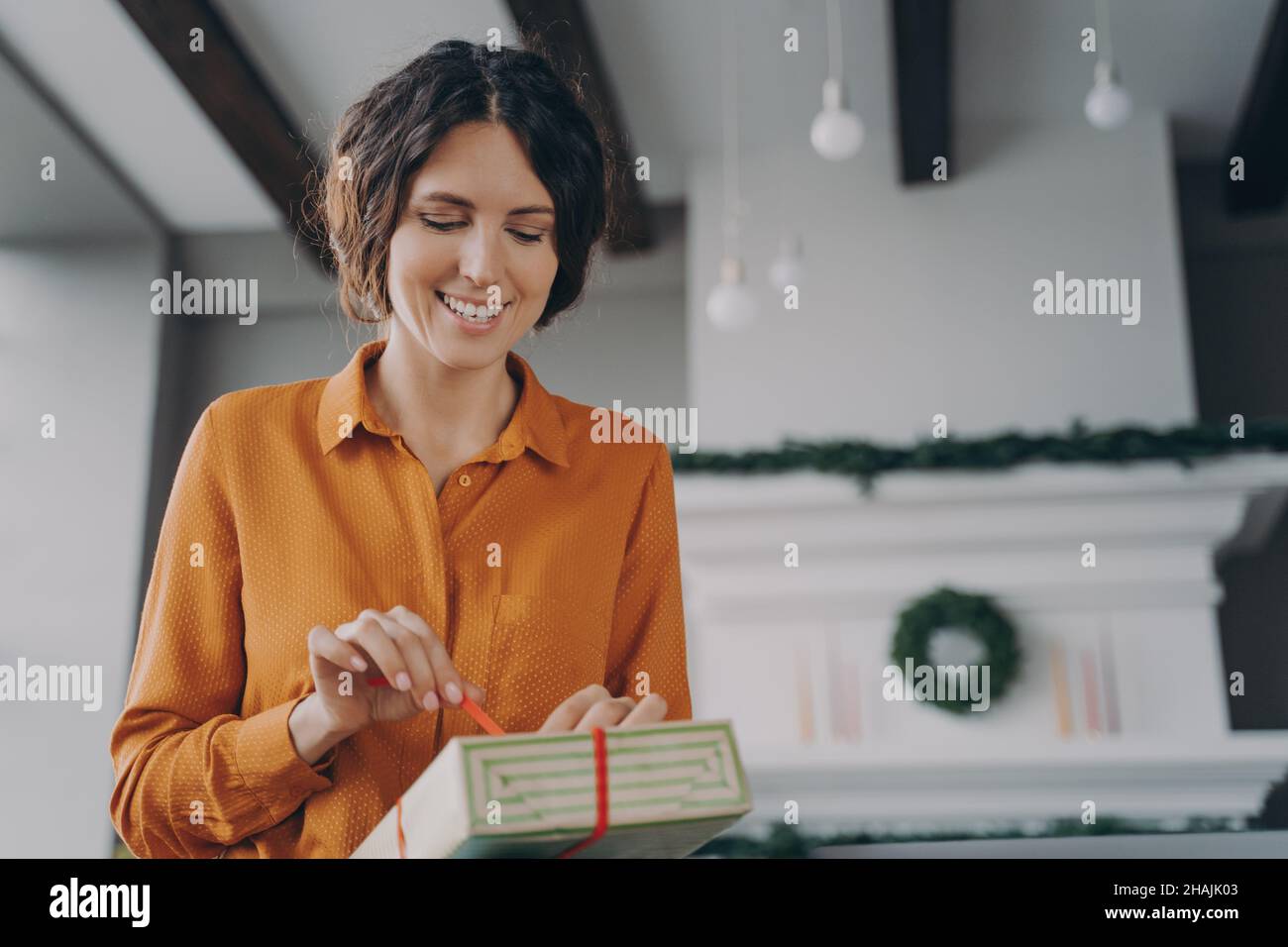 Attractive brunette Italian woman unpacking Christmas present gift box with red bow at home Stock Photo