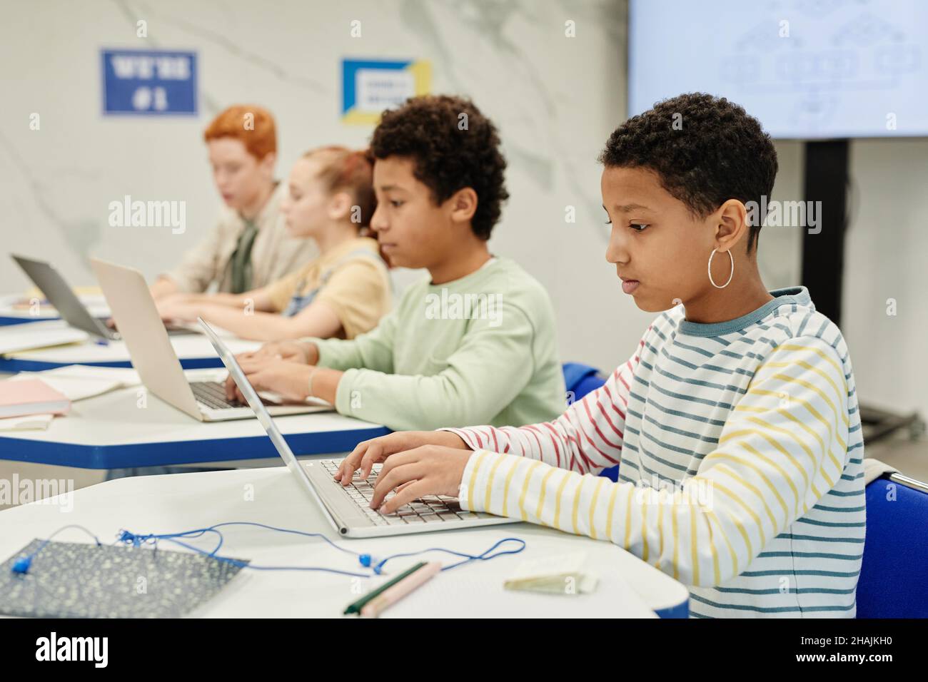 Side view at diverse group of children using laptops at desk in modern classroom, copy space Stock Photo