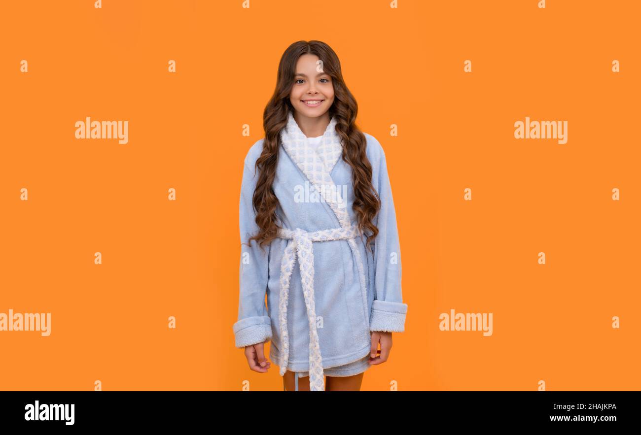 Happy girl child smiling in blue towelling bathrobe orange background, homewear Stock Photo