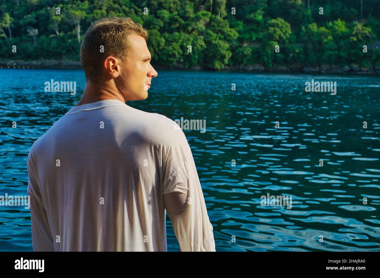 Handsome young bodybuilder by the sea with wet shirt on Stock Photo