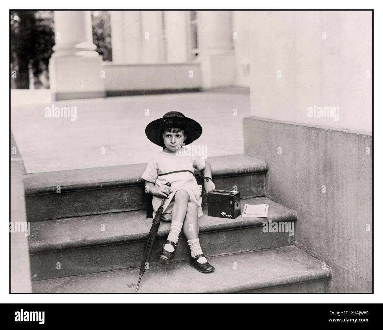 Vintage 1920s 'Waiting for the President' confident young girl with a Kodak Box Camera the latest in amateur photographic technology Photograph shows a girl in a broad brimmed hat seated on the White House steps with an umbrella and a Kodak Box camera by her side. Created / Published 1922 June 29. -  Cameras--1920-1930 -  Children--1920-1930 -  Photography--1920-1930 Little Miss Tarkington, daughter of Mrs. W. Tarkington Jr. Photographed on the steps of the White House patiently waiting to snap a photo of American President Harding Stock Photo