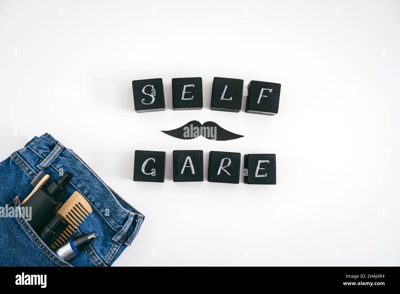 Men self care concept with blue denim jeans and set of male care products and devices and black block with text Self Care on white background. Stock Photo