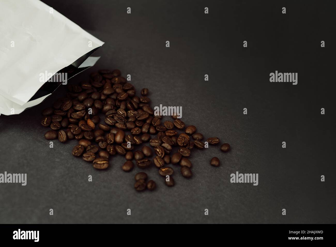 Coffee Beans Spilling out of White Foil Bag on Dark Background with Copy Space Stock Photo