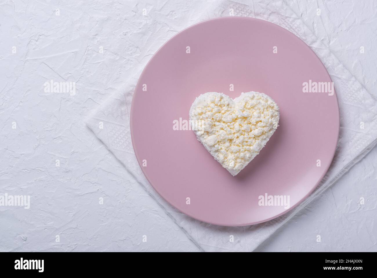 Heart shaped cottage cheese in a pink plate on a white table. Stock Photo