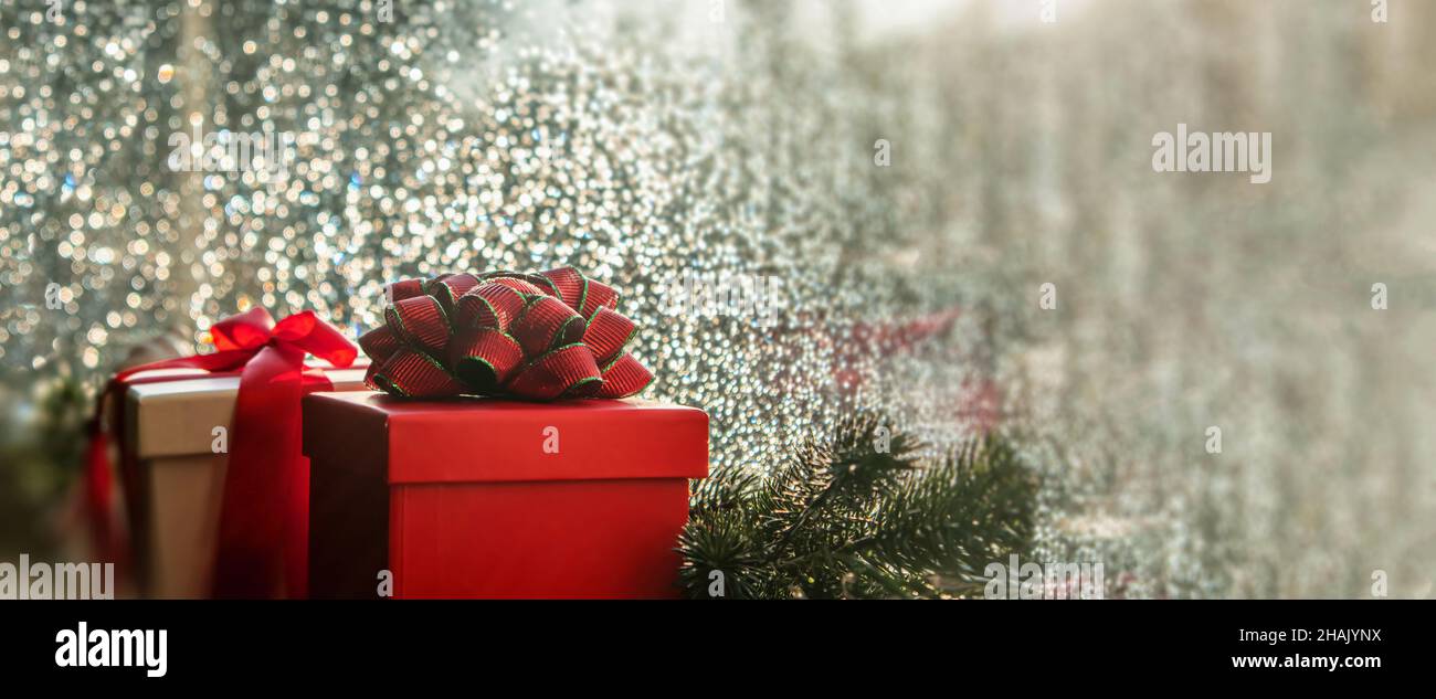 Christmas gift boxes with red ribbon on a window sill. Xmas garland decoration, raindrops on the glass, rainy day. Greeting card template, banner, cop Stock Photo