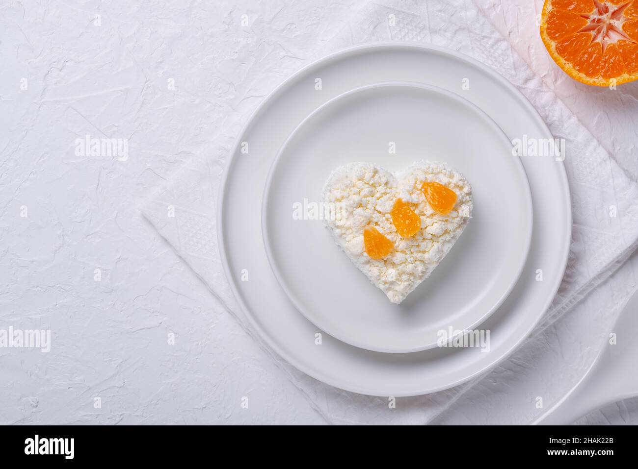 Heart shaped cottage cheese and orange in a plate on a white table. Stock Photo
