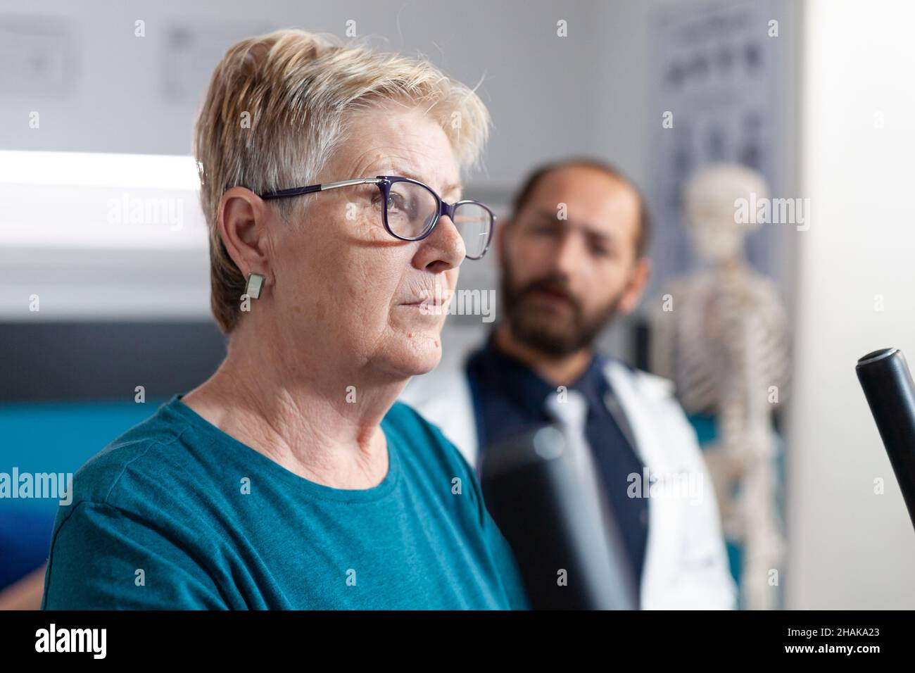 Portrait of retired woman doing physical exercise on bicycle. Close up of senior patient training with sport equipment and gear for recovery. Person at physiotherapy with doctor. Stock Photo