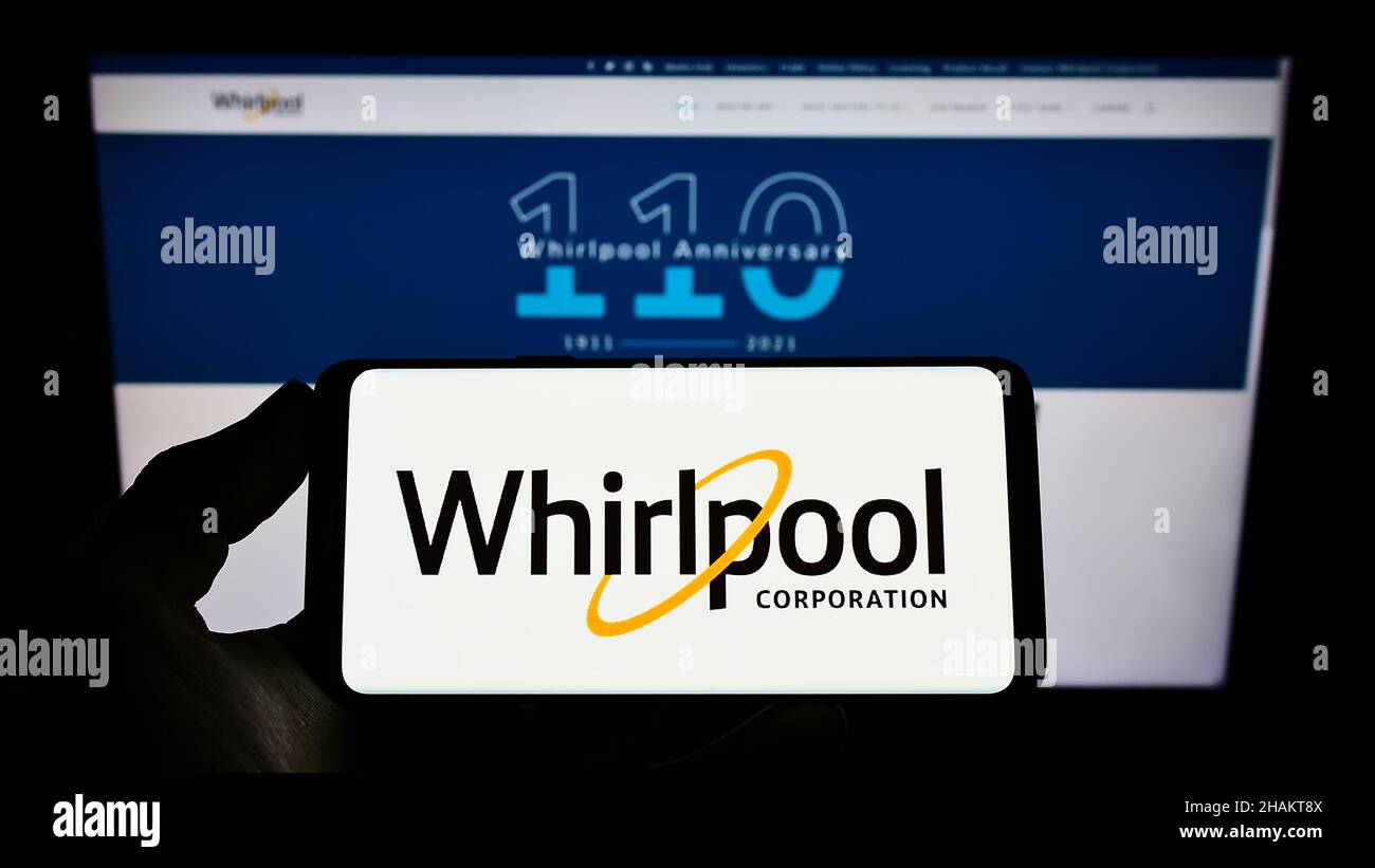 Person holding cellphone with logo of American home appliances company Whirlpool Corporation on screen in front of webpage. Focus on phone display. Stock Photo