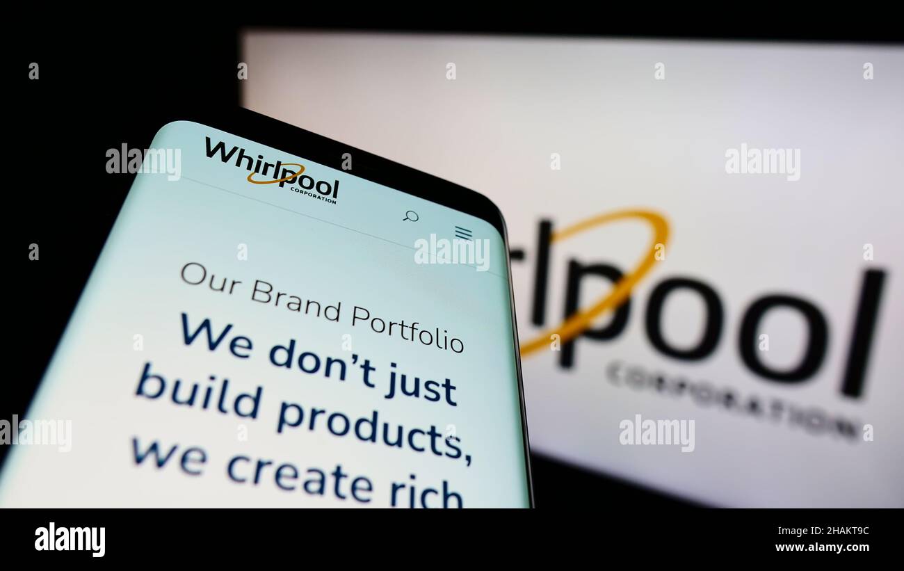 Mobile phone with webpage of American home appliances company Whirlpool Corporation on screen in front of logo. Focus on top-left of phone display. Stock Photo