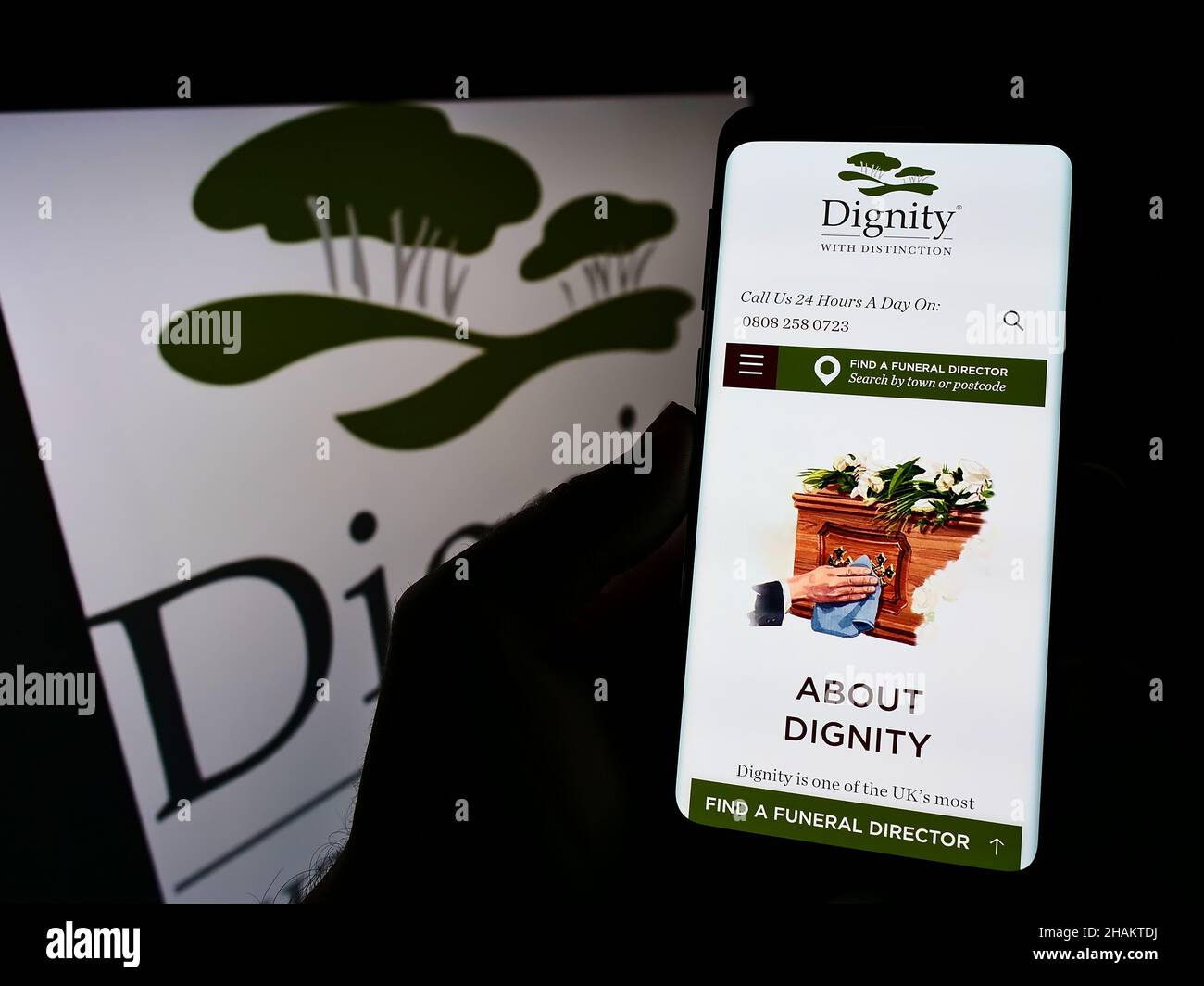 Person holding cellphone with webpage of British funeral services company Dignity plc on screen with logo. Focus on center of phone display. Stock Photo