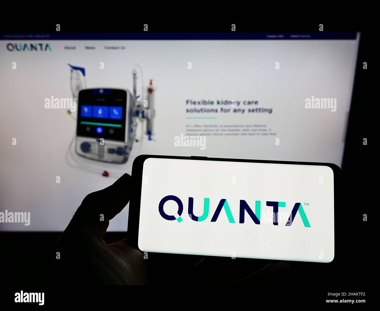 Person holding cellphone with logo of British company Quanta Dialysis Technologies Limited on screen in front of webpage. Focus on phone display. Stock Photo