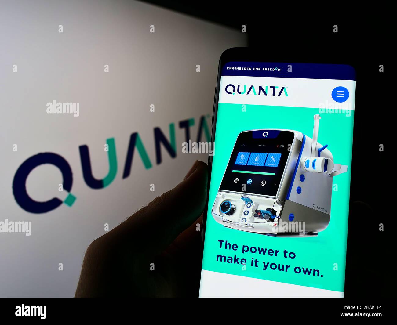 Person holding smartphone with website of company Quanta Dialysis Technologies Limited on screen with logo. Focus on center of phone display. Stock Photo