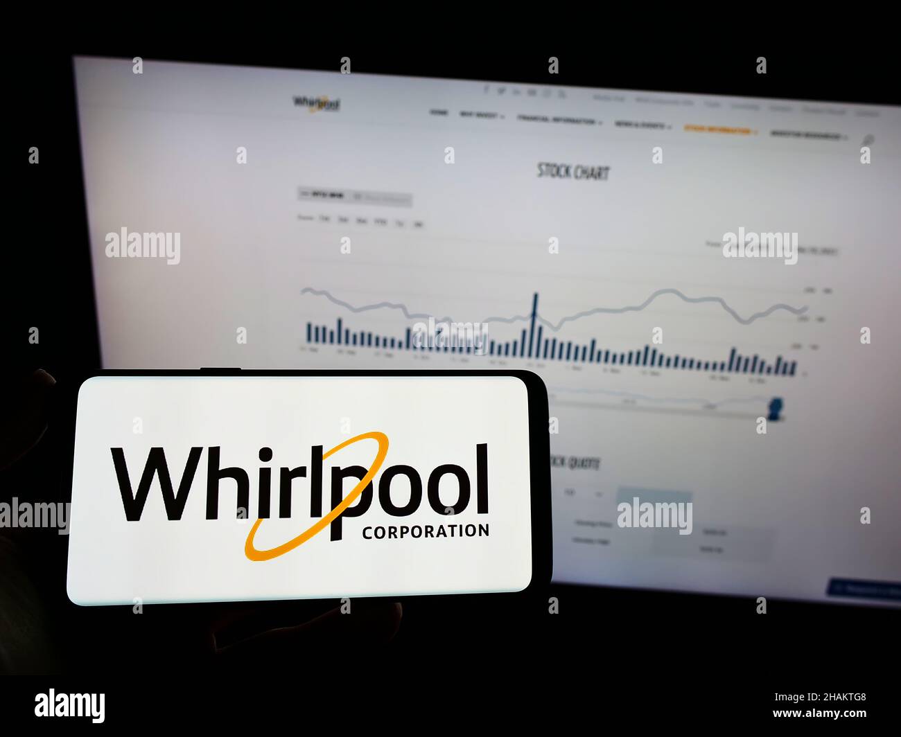 Person holding mobile phone with logo of US home appliances company Whirlpool Corporation on screen in front of web page. Focus on phone display. Stock Photo