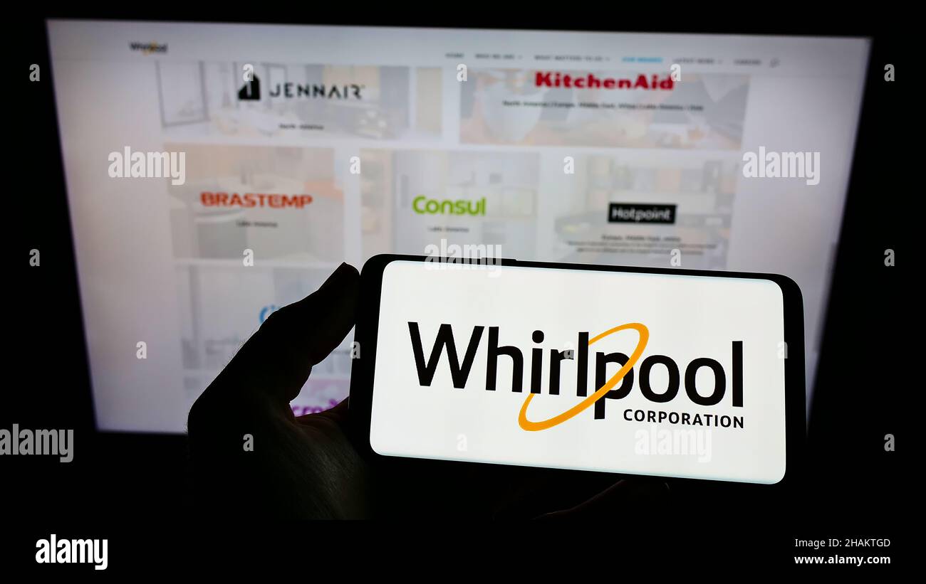 Person holding smartphone with logo of US home appliances company Whirlpool Corporation on screen in front of website. Focus on phone display. Stock Photo