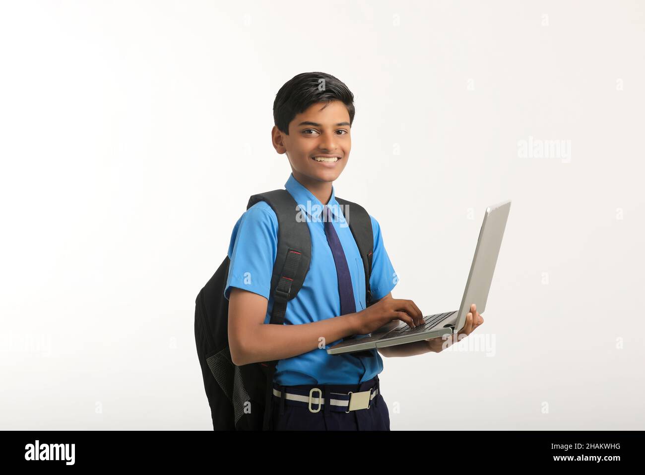Indian school boy in uniform and using laptop on white background. Stock Photo