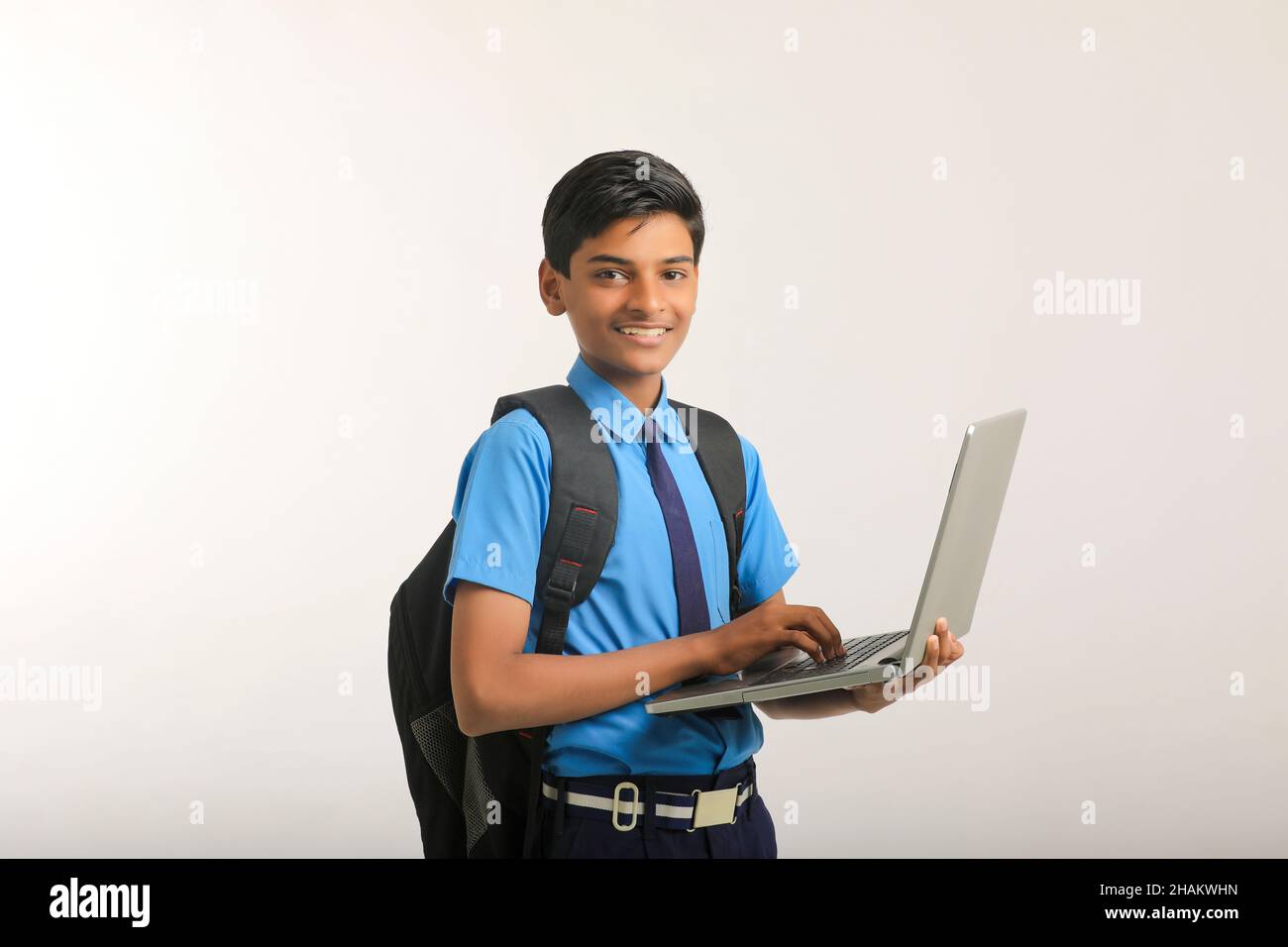 Indian school boy in uniform and using laptop on white background. Stock Photo