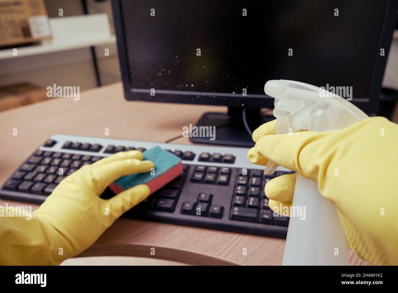 Cleaning the office, a janitor in yellow gloves wipes keyboard and ...