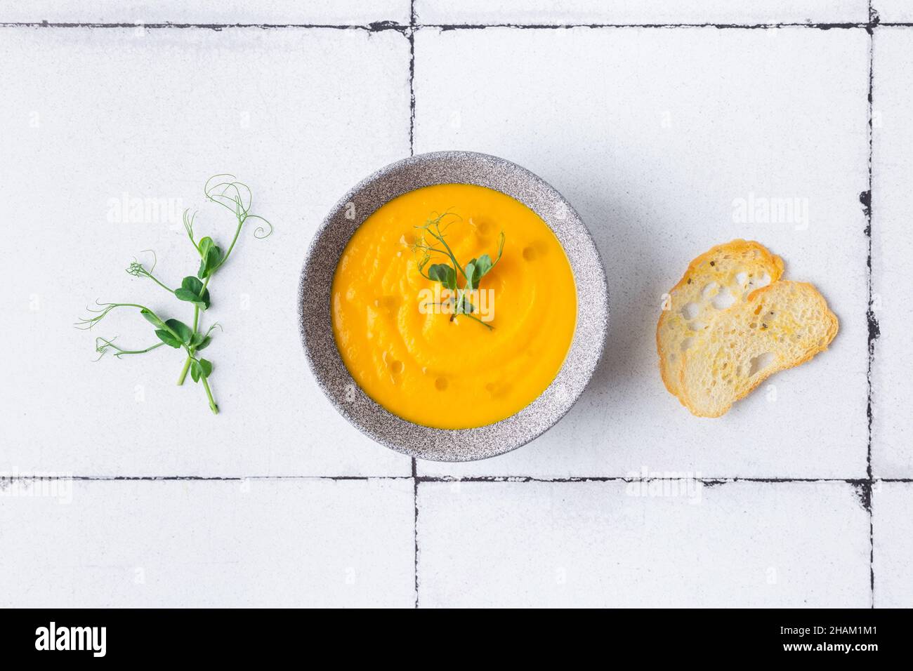 Pumpkin and carrot cream soup on white tile background with croutons. Top view. Stock Photo