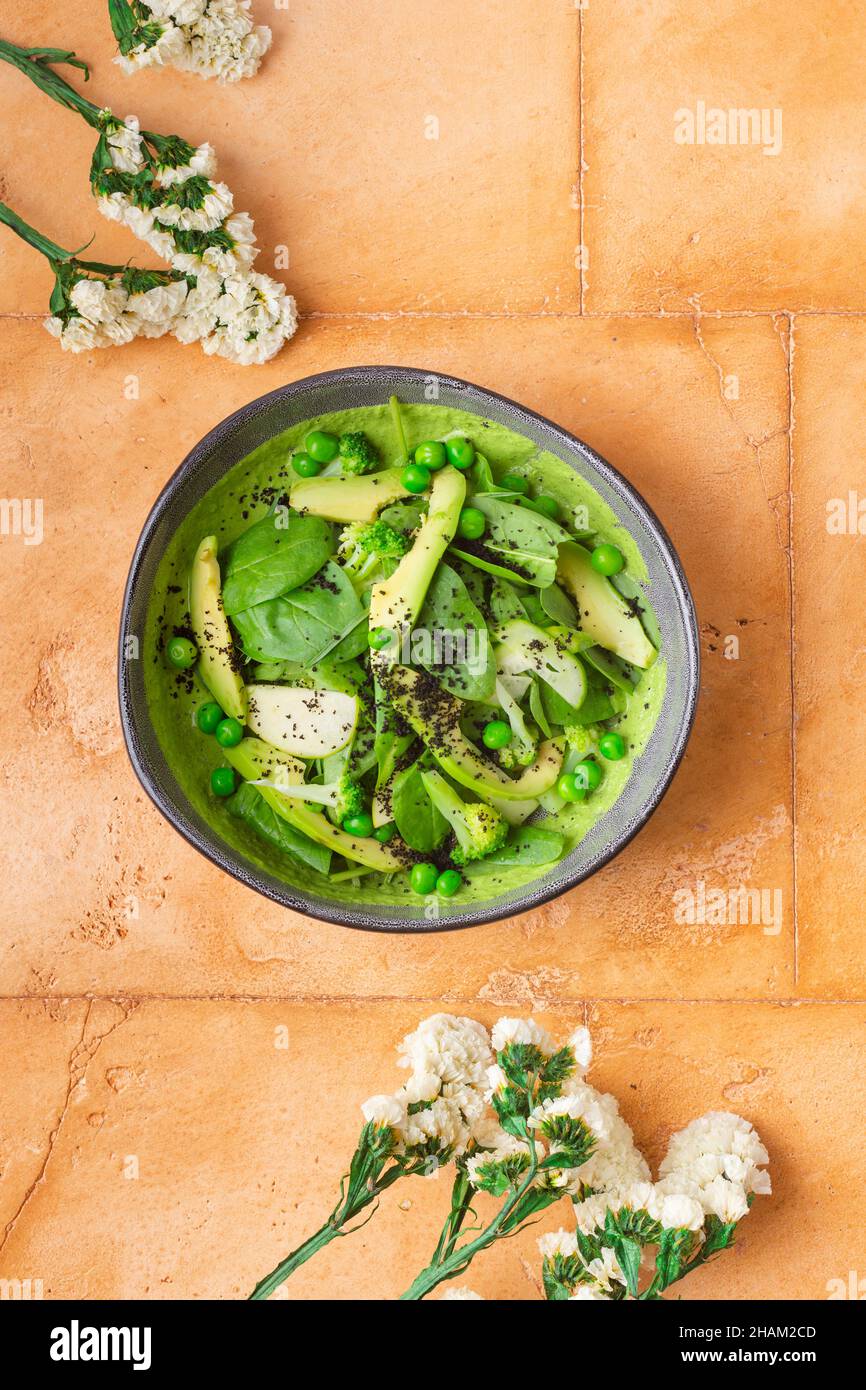Green smoothie bowl with avocado pies spinach on brown background with flowers Stock Photo