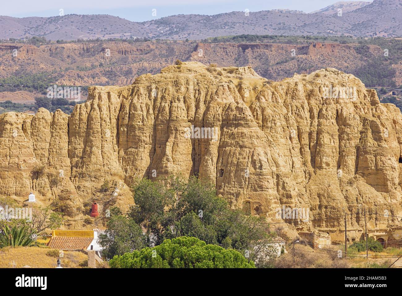 Tuff formations with troglodyte habitations to protect from the heat in Guadix. The heat causes a blurry view for the distant mountains. Stock Photo