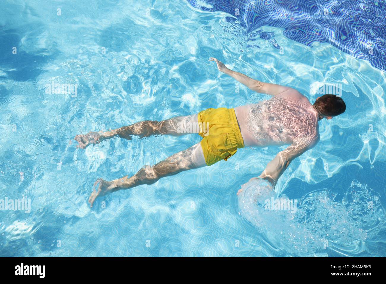 Male person in swimming pants floating on water on belly, clear water in pool Stock Photo
