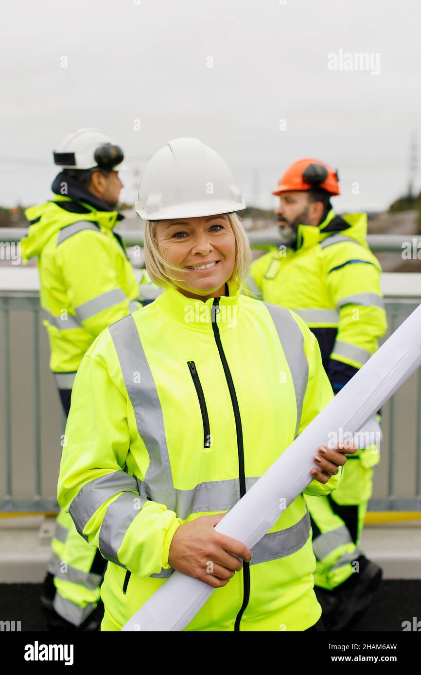 Engineers in reflective clothing standing on bridge with blueprints