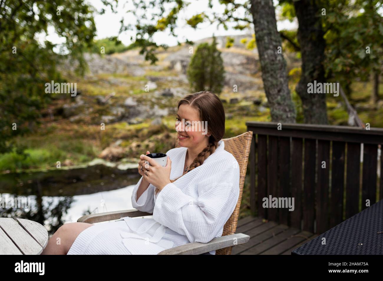 Smiling young woman in bathrobe sitting on deck Stock Photo