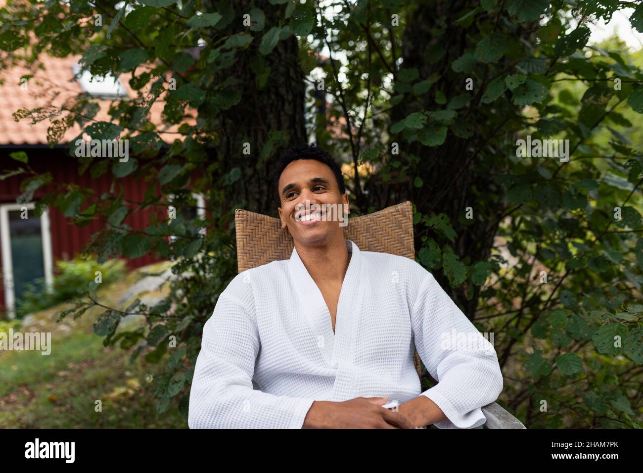 Smiling young man in bathrobe sitting outdoors Stock Photo
