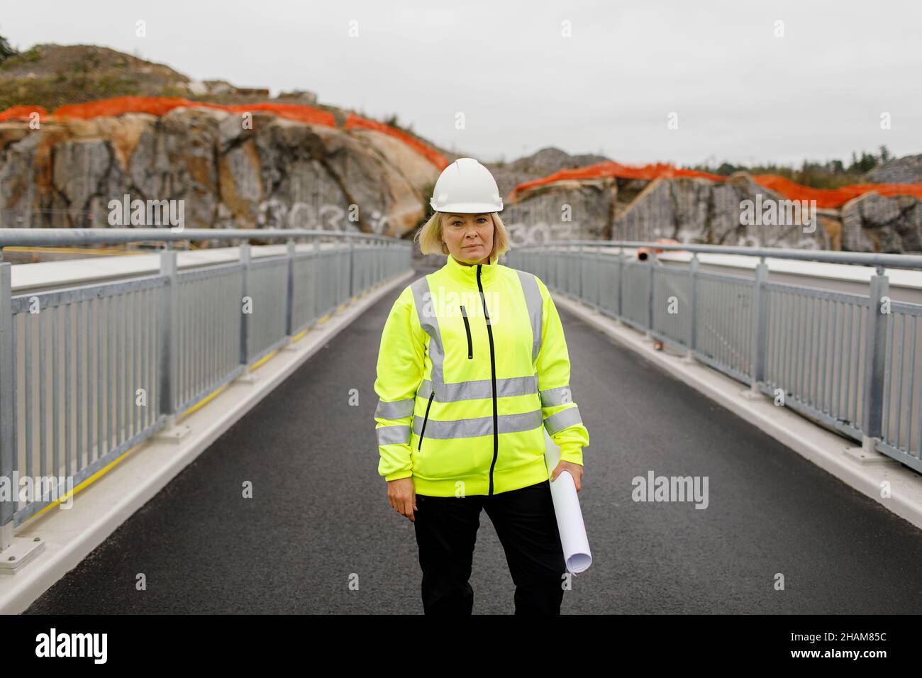 Portrait of female engineer in reflecting clothing standing on bridge Stock Photo