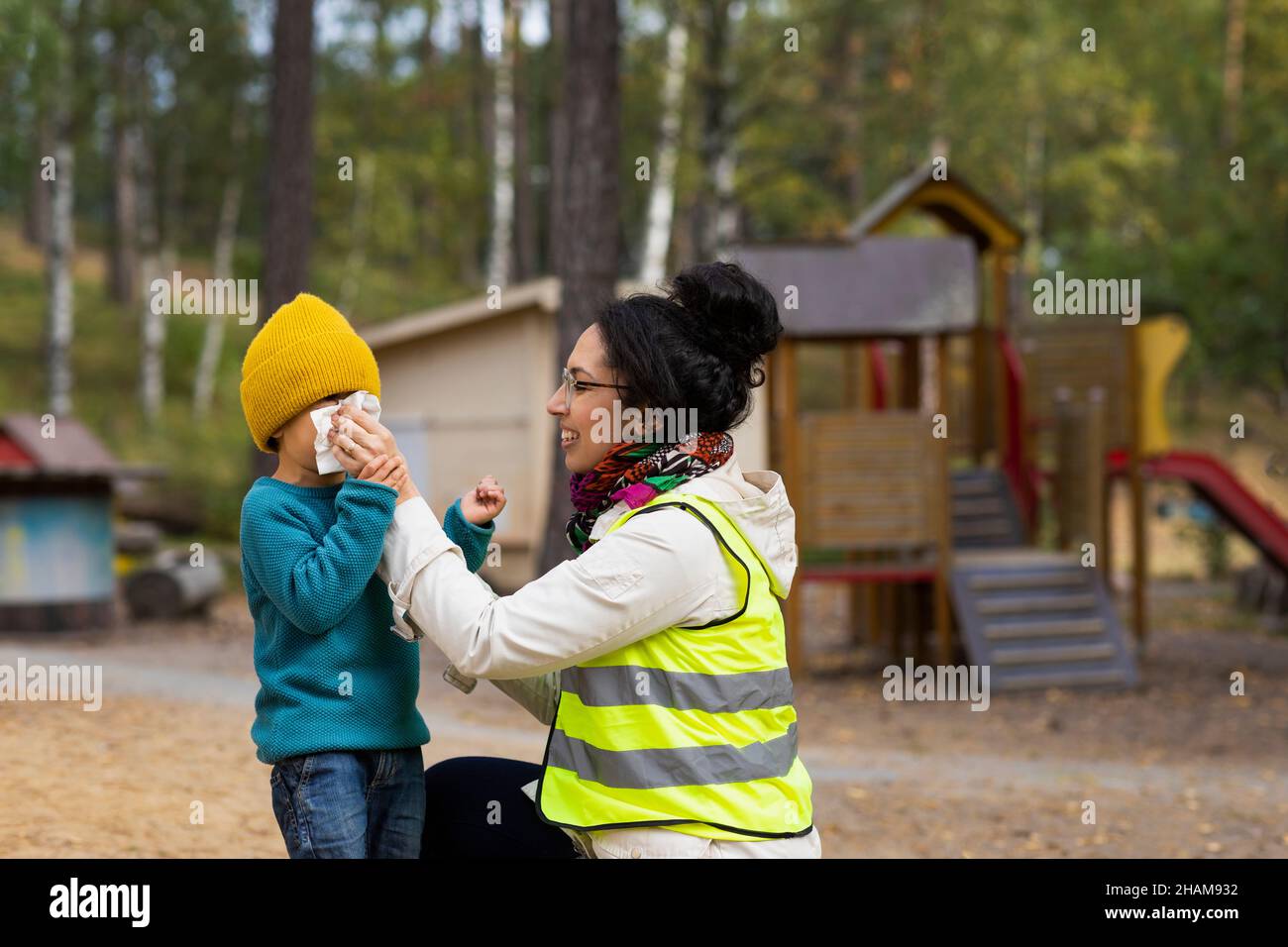 Preschool teacher helping student blow nose at playground Stock Photo