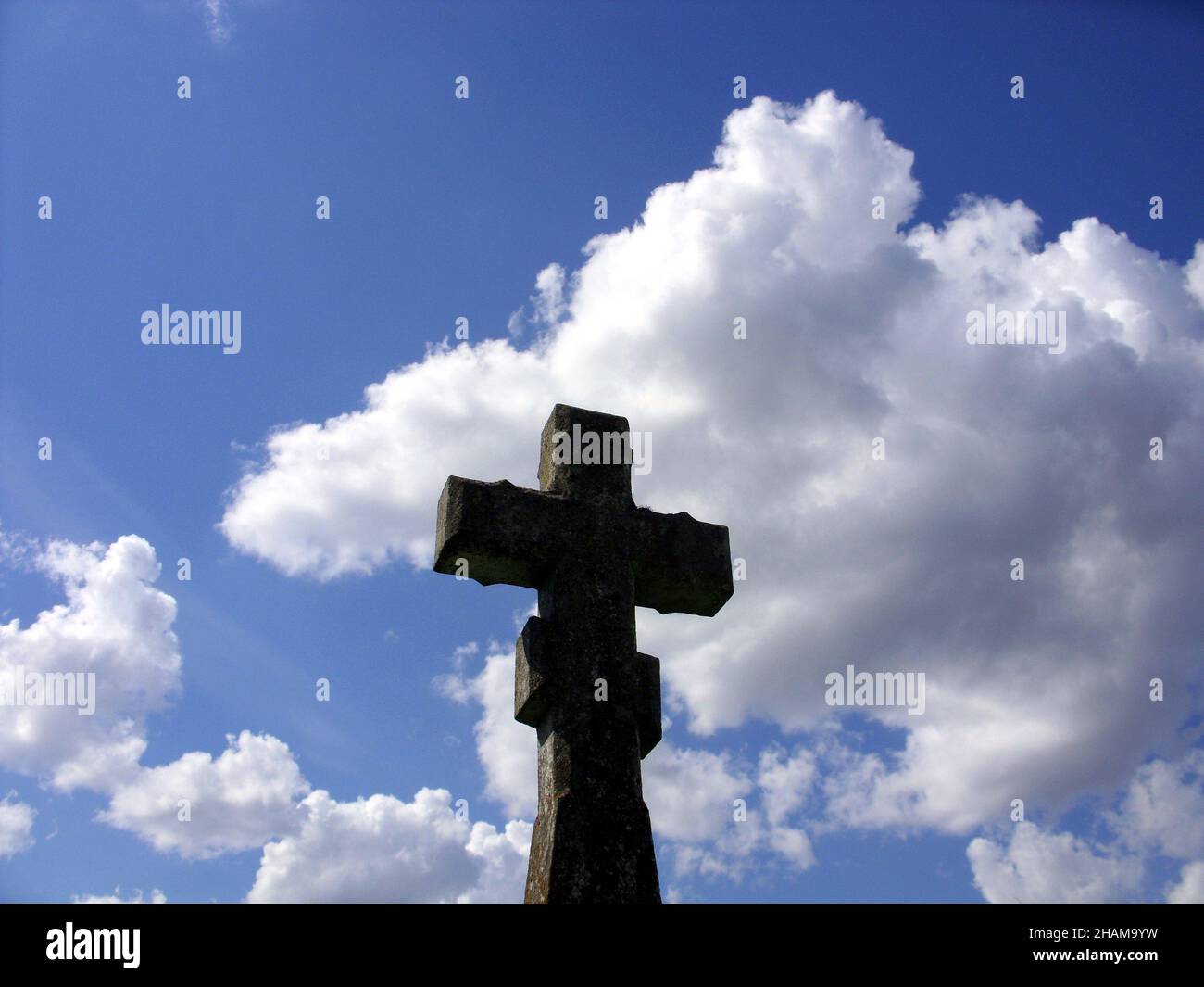Lonely stone cross at an old graveyard, summer sky, back light Stock Photo