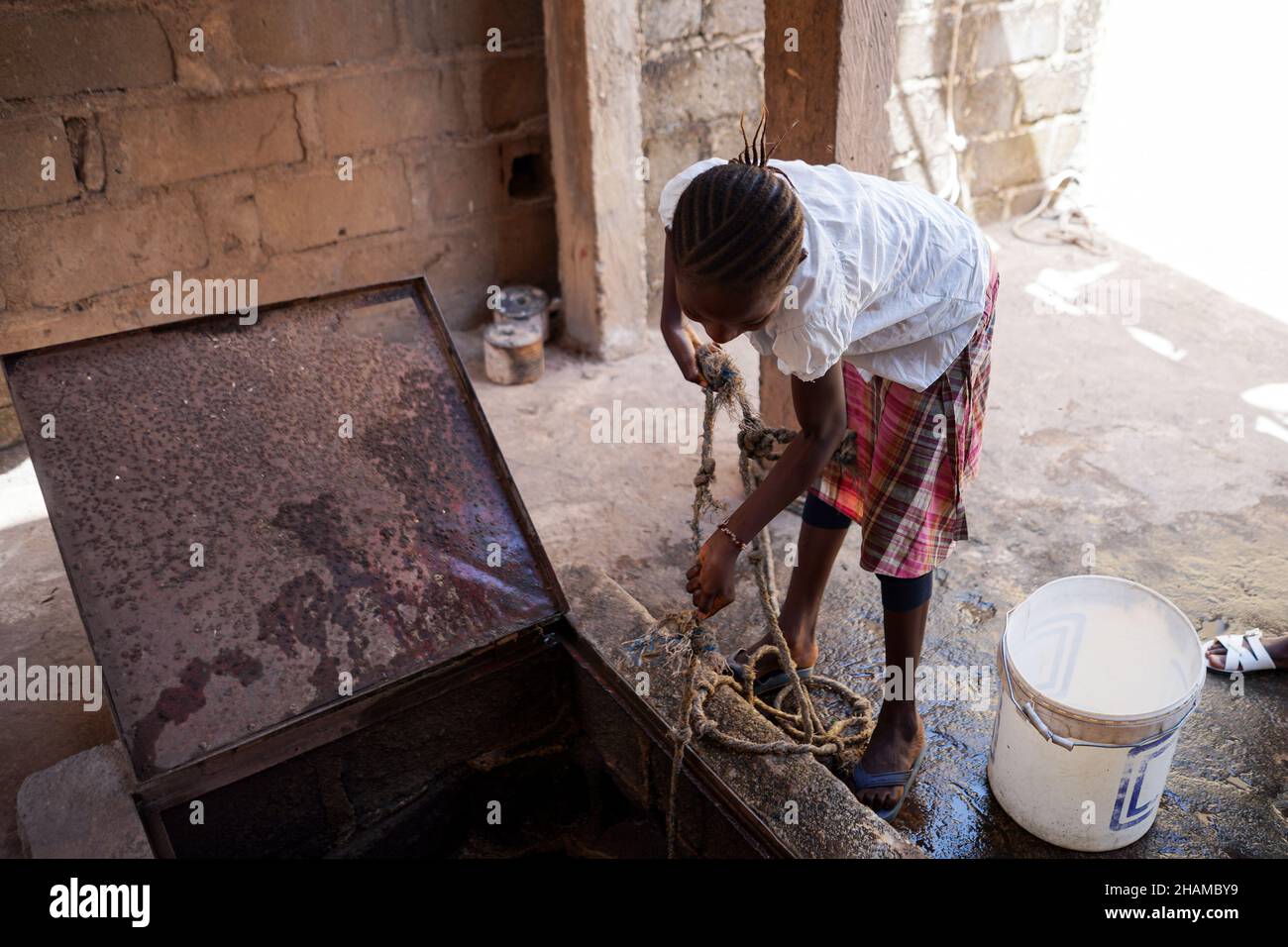 Thirsty african young person drawing water from well indoors with