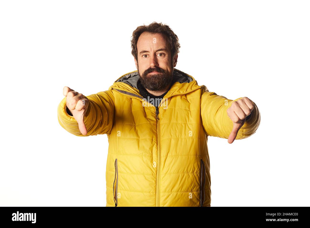 Puzzled bearded man guy in yellow casual jacket isolated on white background, thumb down fingers Stock Photo