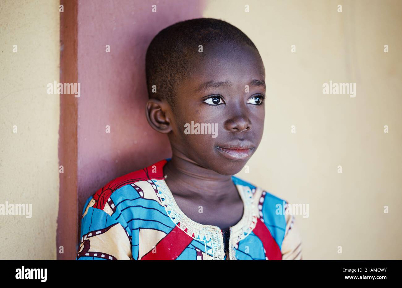 Portrait of young adorable shaved-head african boy look away to side by wall in rural Africa Stock Photo