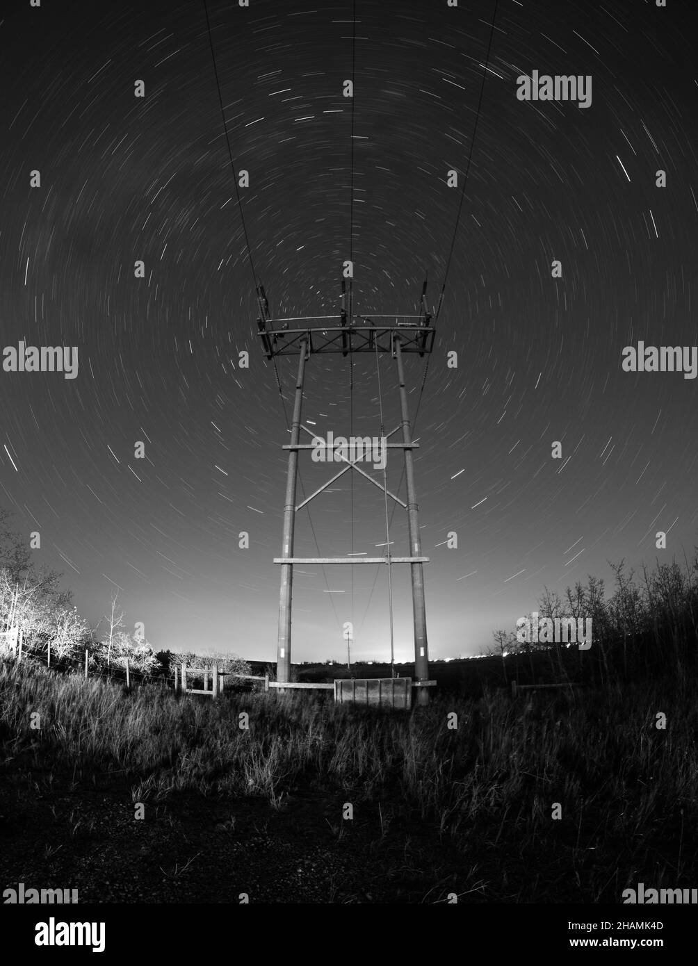 AIRDRIE, CANADA - Nov 17, 2021: A vertical grayscale shot of an electricity tower under a night sky with star trails Stock Photo