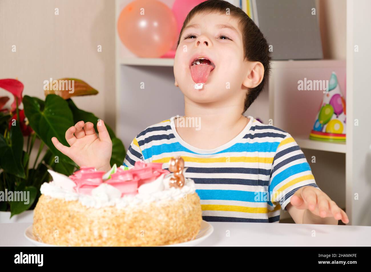 The child celebrates a birthday, laughs and licks, eats a birthday cake. Stock Photo