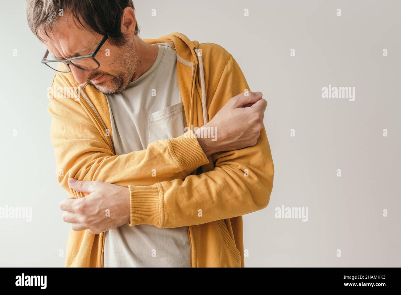 Aching elbow as symptom of tendinitis, adult caucasian male with painful grimace looking down at his joint Stock Photo