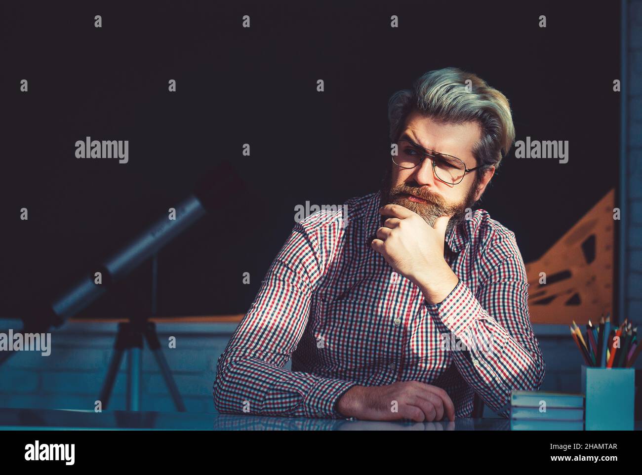 Young male teacher with books sitting at table in classroom. Stock Photo