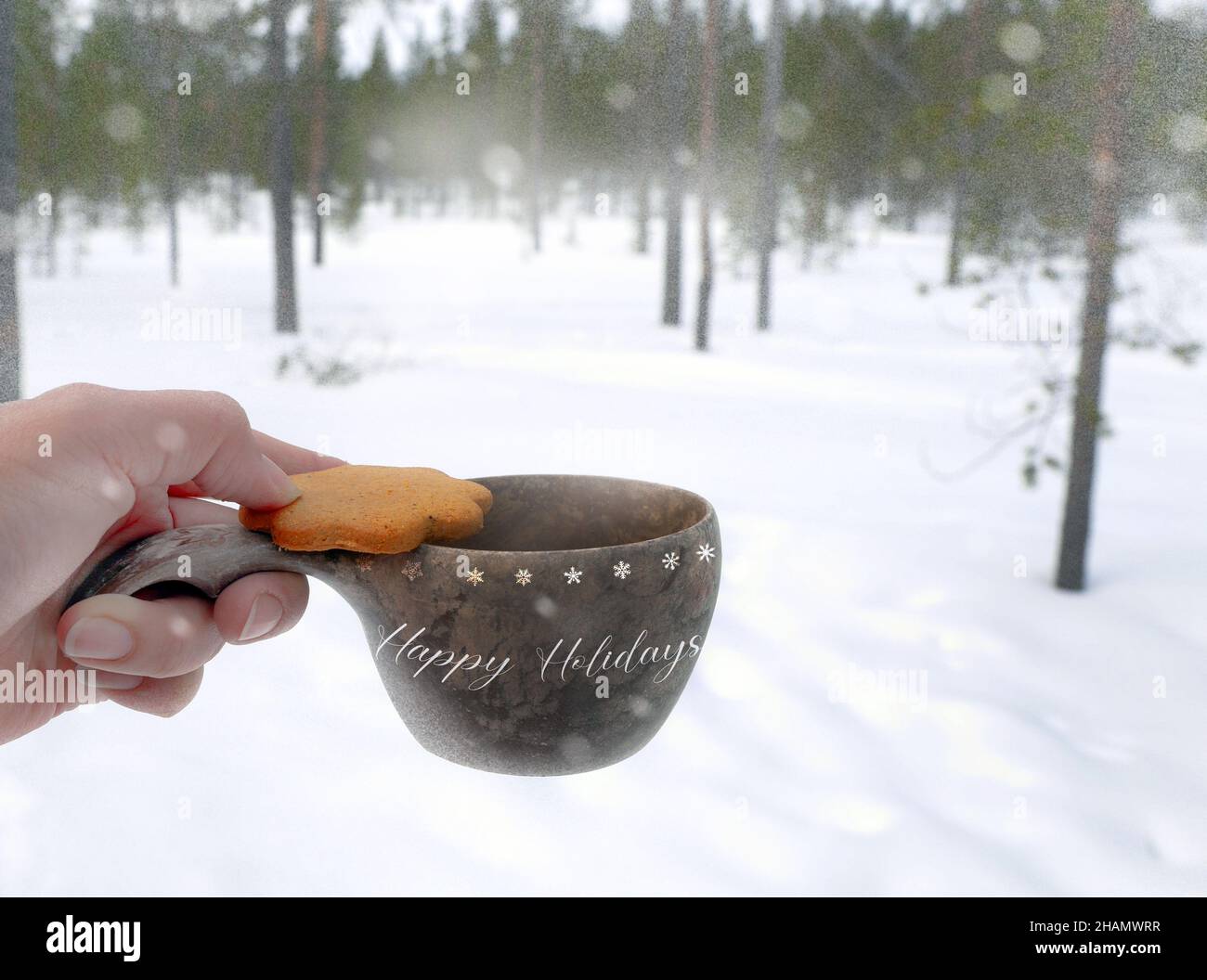 a hand holding biscuit cookie with warm drink in a wooden cup outside with the pine tree forest view under cover of white snowing happy holidays Stock Photo