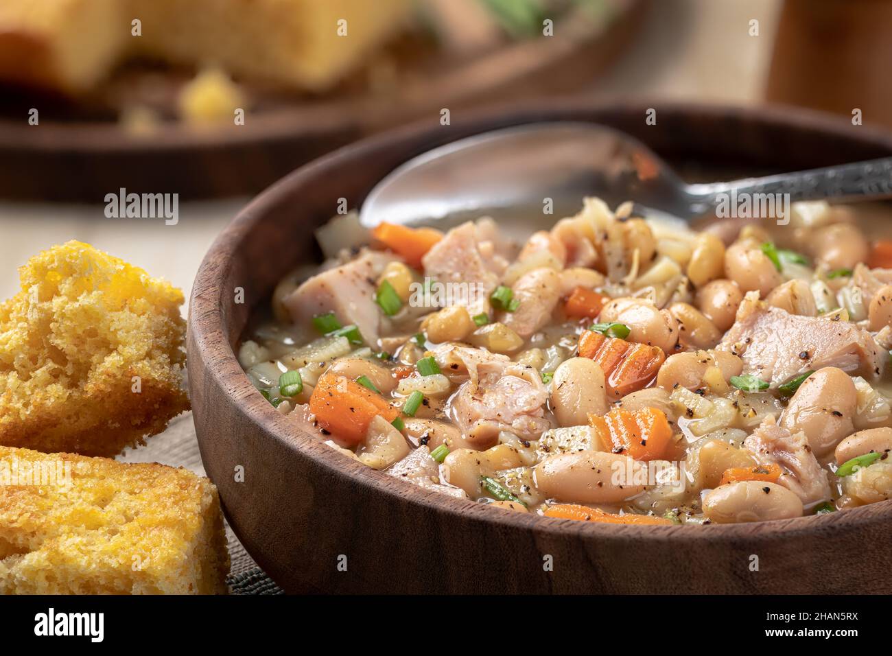 Ham and bean soup with carrots and chives in a wooden bowl with cornbread on a rustic wooden table closeup Stock Photo