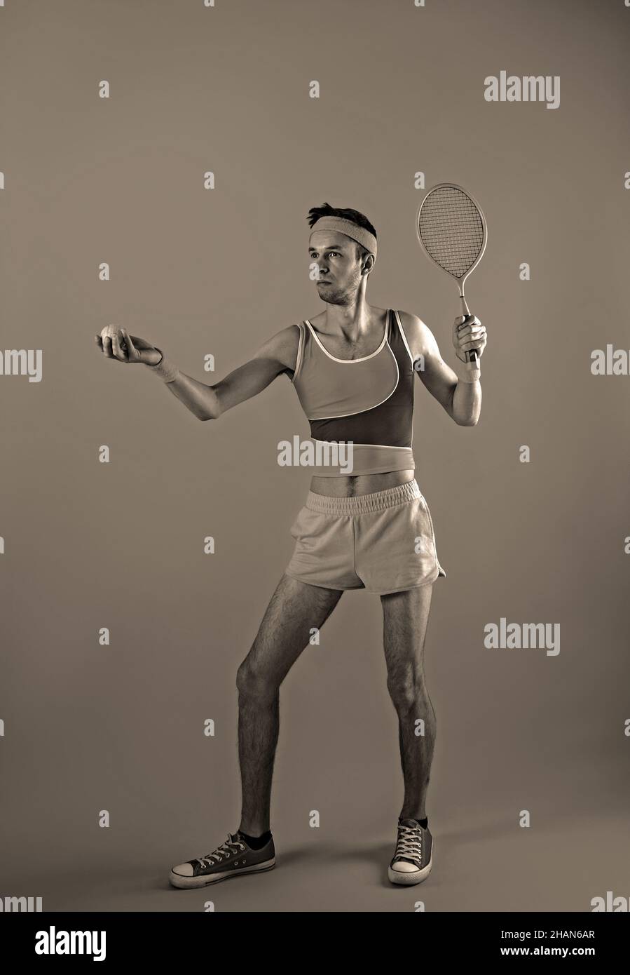 Funny playful young man tennis player with racket imitating ball serve